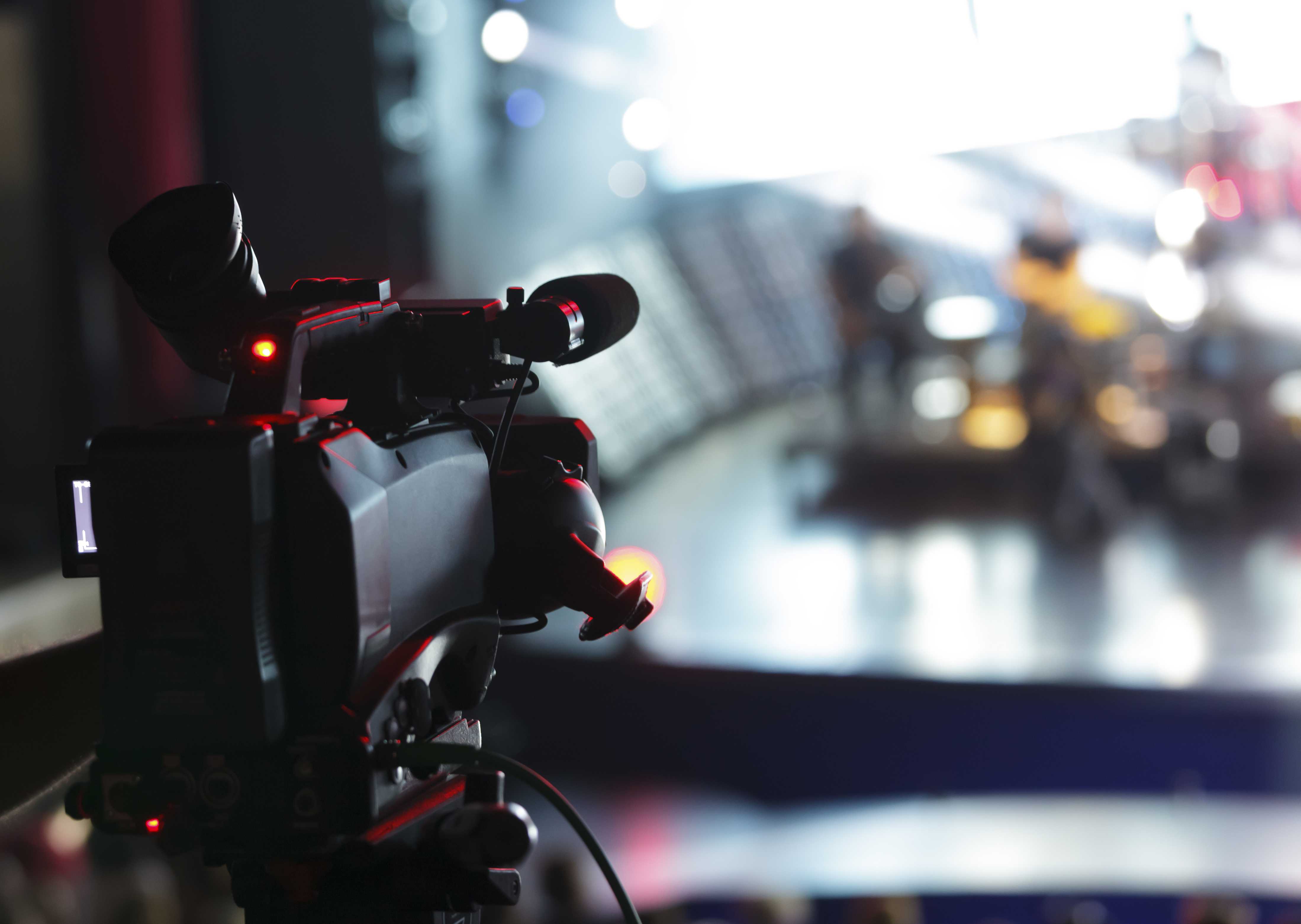 A professional video camera on a stand in a dark venue with blurred bright stage lights, dramatic performance atmosphere